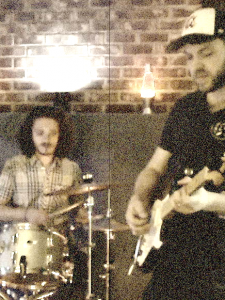 A picture of Seth playing guitar in a vibe-a-licious room while Kevin lays down that fat beat on a vintage Ludwig drum set!